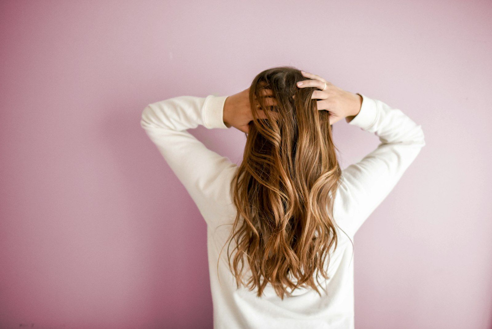 Long, glossy wavy hair seen from behind against a blush wall
