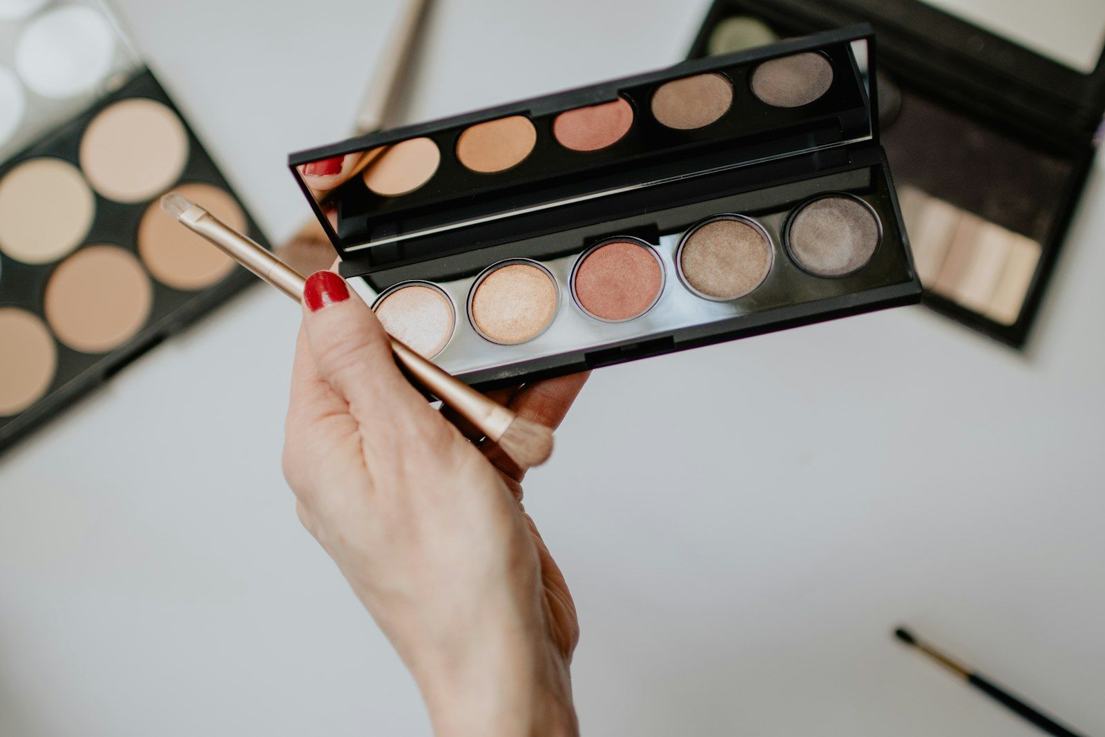 A hand holding an eyeshadow palette and brush